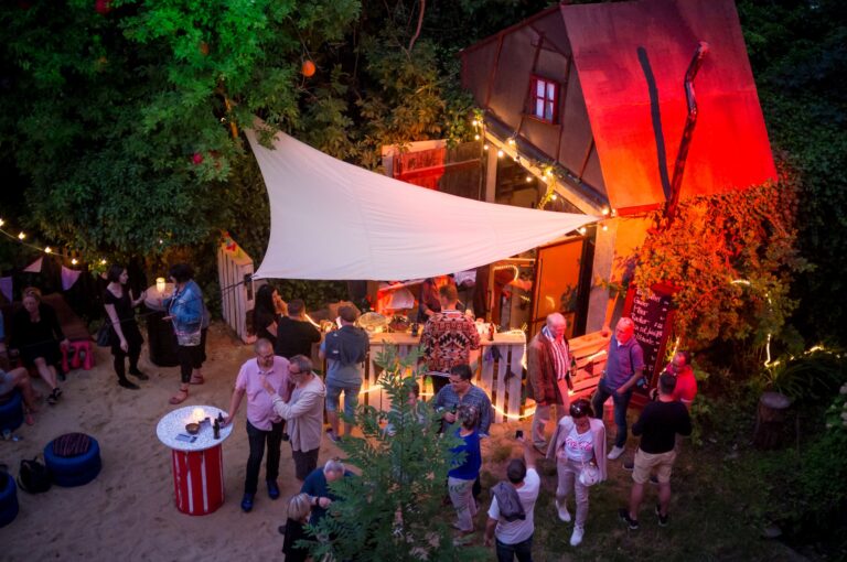 Hof bei Nacht mit Sonnensegel, Lichterketten und Gästen