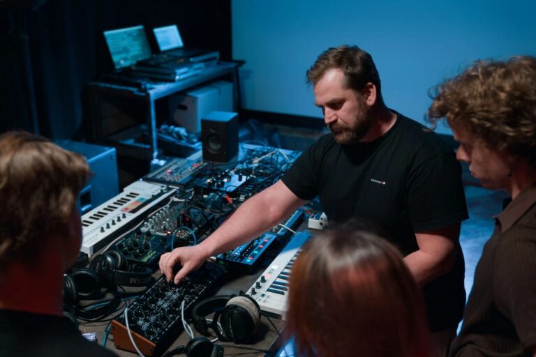 Ein Musiker zeigt Zuhörenden sein Setup aus Synthesizern und Drumcomputern
